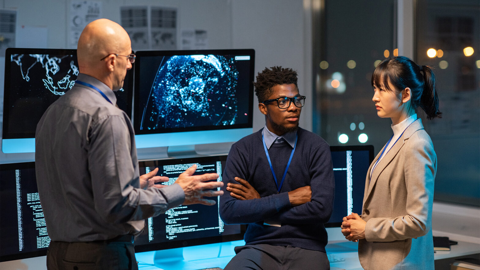 Three intercultural colleagues in formalwear discussing working points at meeting by their workplace in openspace office